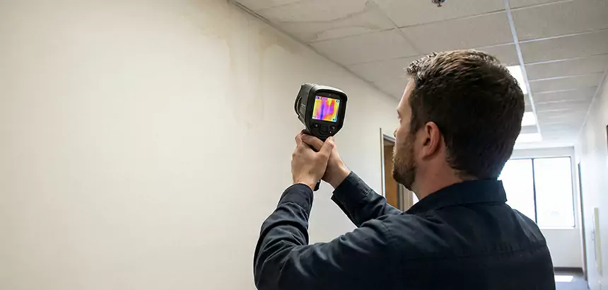 Technician using a thermal imaging camera to check moisture near a ceiling leak.